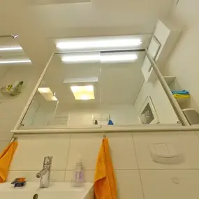 Modernes Badezimmer mit großer Spiegelwand, Dusche, Waschbecken und gelben Handtüchern.