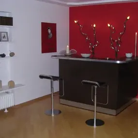 Moderne Hausbar mit dunkler Theke, roten Wänden, Barhockern und stilvollen Kerzenhaltern.