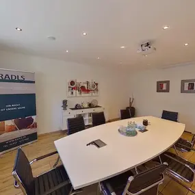 Moderner Konferenzraum mit großem Besprechungstisch, Stühlen und Kanzlei-Rollup.