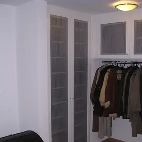 Eingebaute Garderobe mit Gittertüren, Kleiderstange und Jacken in modernem Flur.