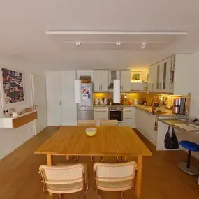 Moderne Einbauküche mit Esstisch, hellen Möbeln, Arbeitsbereich und Holzfußboden.