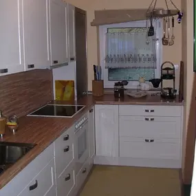 Moderne Einbauküche mit weißen Schränken, Holzarbeitsplatte und Küchengeräten.