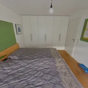 Modernes Schlafzimmer mit Doppelbett, grünem Wandakzent, großem Kleiderschrank und Pinnwand.