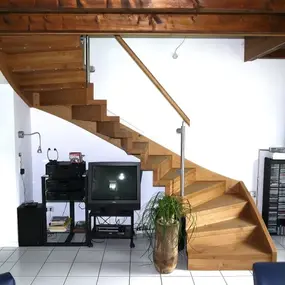 Moderne Holztreppe im Wohnzimmer mit TV, Hifi-Anlage, Zimmerpflanze und Regalen.