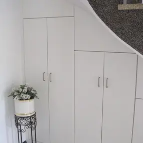 Einbauschrank unter Treppe mit weißen Türen und Griffen, daneben Blumentopf mit Gänseblümchen.